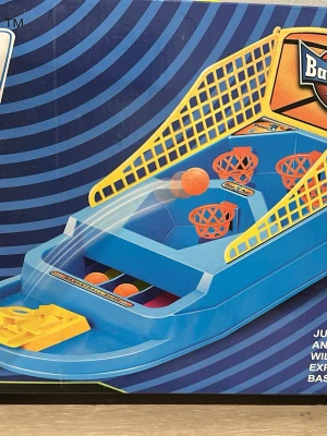 Blå basketspel i plast - Roligt basketspel i blå plast med tre orangea korgar och gula sidonät. Spelet har en gul avfyrningsmekanism och små orangea bollar. Perfekt för att utmana vänner och testa sina basketkunskaper hemma.