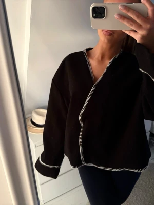 Svart kappa/kofta - Så fin svart kappa med vita sömmar perfekt till våren 🌺endast använd några gånger så i väldigt fint skick ☺️funkar som både jacka och kofta 🎀passar alla storlekar beroende på hur stort man vill att den ska sitta!