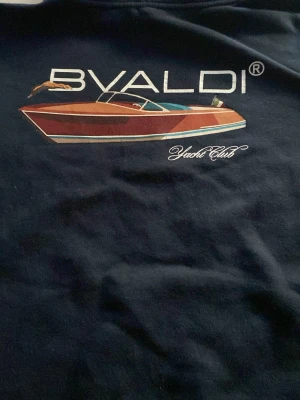 Marinblå hoodie från Bvaldi Yacht Club - Snygg marinblå hoodie från Bvaldi Yacht Club med tryck av en båt och text på bröstet. Den är ny och inte använd eftersom köpte fel storlek den är XS men passar S