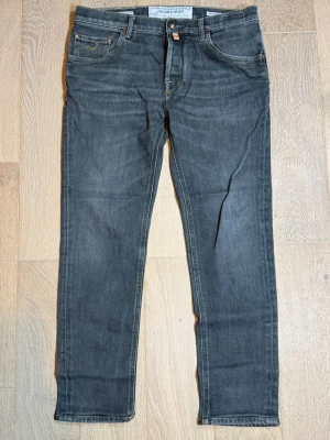 Grå jeans från Jacob Cohën - Snygga grå jeans från Jacob Cohën med klassisk femficksmodell och raka ben. Jeansen har kontrastsömmar och patch med logga bak i midjan. Tillverkade i mjukt denimtyg som ger en skön känsla och stilren look. W32 längd 93cm