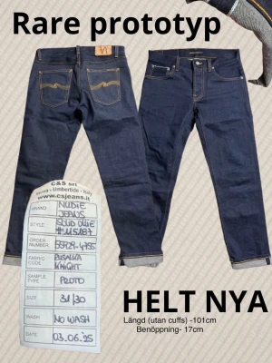 Title: RARE Nudie Jeans Prototype - "Solid Ollie" - Deadstock/New - Sample - Extremely rare opportunity to own a piece of Nudie Jeans history. This is a factory prototype/sample produced at the C&S srl factory in Italy (Umbertide). • Model: Solid Ollie (Rare/Prototype cut) • Fabric: "Pusalka Knight" (Unique sample fabric) • Condition: Brand New / Deadstock (No wash) • Details: Features the original handwritten sample tag from the factory dated 03.06.25. • Measurements: * Size: W31 / L30 • Length (uncuffed): 101 cm • Leg opening: 17 cm Perfect for collectors 