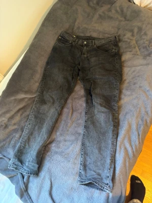 Mörkgråa Levis jeans - Säljer ett par svarta Levi's jeans med klassisk straight fit och femficksmodell. Jeansen har en diskret tvättad look och är tillverkade i slitstark denim. Passar perfekt till en avslappnad stil och har den ikoniska läderlappen bak i midjan. Bältet har färgat av sig som ses på sista bilden men inga defekter utöver det