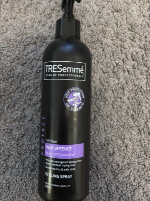 TRESemmé Heat Defence Styling Spray - TRESemmé Heat Defence Styling Spray med UV-filter skyddar håret mot värme upp till 230°C. Svart plastflaska med spraymunstycke och lila detaljer. Perfekt för att minska friss och ge glans vid användning av värmeverktyg.