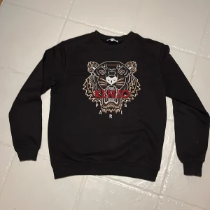 Svart sweatshirt från Kenzo som passar xs - Säljer en svart sweatshirt från Kenzo med ett stort tigertryck och texten 'Kenzo Paris' på framsidan. Tröjan har långa ärmar och rund halsringning. Perfekt för en stilren och trendig look. Storlek m men passar lite som en small. Knappast använd