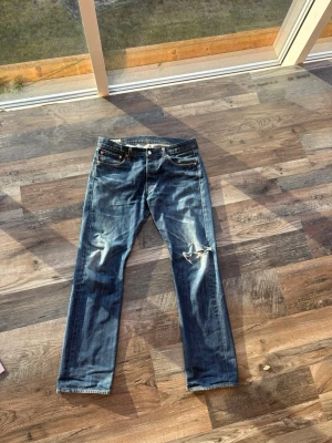 Blå vintage 501or - Säljer ett par blå jeans med raka ben och tydliga slitningar på knäet. Jeansen har klassisk femficksdesign och är gjorda i denim med en snygg tvätt. Perfekta för en avslappnad och trendig look. Storleken är 33/32 men sitter snyggt även om du har 30-32 i midjan  också