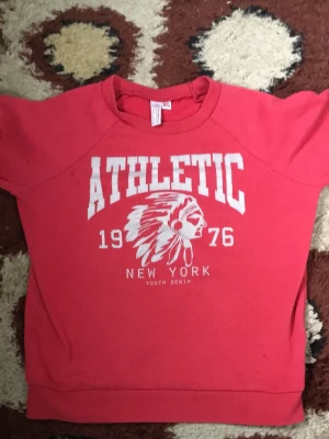 Röd sweatshirt ATHLETIC från Woxo - Cool röd sweatshirt från Woxo med trycket ATHLETIC, 1976 och New York framtill. Tröjan har rund halsringning och långa ärmar. Mjuk insida och avslappnad passform, perfekt för en chill look ogräs Ike kort