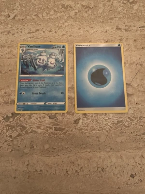 Pokémonkort Vanilluxe + Vattenenergi - Två Pokémonkort säljes: ett Vanilluxe-kort med blå bakgrund och ismotiv samt ett vattenenergikort med blått vatten-symbol. Båda korten har klassisk Pokémon-design med gul ram och tryckt text. Perfekt till samlingen eller spelkvällar!