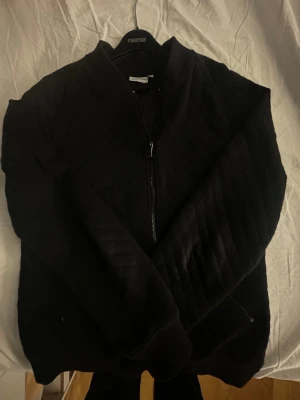 Svart zip hoodie från J.Lindeberg - Snygg svart hoodie från J.Lindeberg med dragkedja framtill och ribbade muddar. 