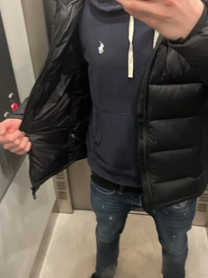 Mörkblå hoodie från Polo Ralph Lauren - Snygg mörkblå hoodie från Polo Ralph Lauren med vit dragsko i huvan och klassisk logga broderad på bröstet. Hoodien har en stor magficka och ribbade muddar vid ärmar och midja. Tillverkad i mjuk bomullsblandning för skön känsla.