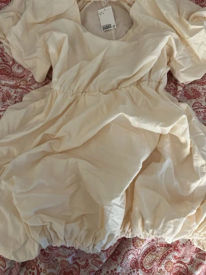 Ljus kort klänning från H&M - Supersöt ljus kort klänning från H&M med puffärmar och markerad midja. Klänningen har en luftig och voluminös kjol samt v-ringad hals. Perfekt för dig som gillar en romantisk och trendig stil.