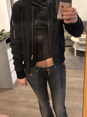 Svart bomberjacka från STAY XS - Snygg svart bomberjacka från STAY Scandinavian Esthetics i storlek XS. Klassisk modell med dragkedja framtill, ribbade muddar och ärmficka med dragkedja. Perfekt för en cool och avslappnad stil.