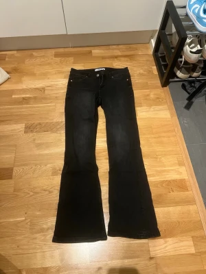 Svarta bootcut jeans från Kappahl - Snygga svarta bootcut jeans från Kappahl med klassisk femficksdesign och kopparfärgade nitar. Jeansen har utsvängda ben och normal midja, perfekta för en trendig och avslappnad look. Materialet är denim med stretch för extra komfort.
