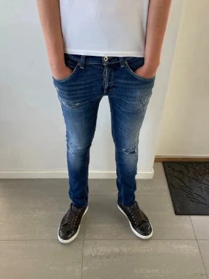Blå slim fit jeans med slitningar - Snygga blå slim fit jeans med slitna detaljer på knäna och låren. Jeansen har klassisk femficksdesign, låg midja och smal passform. Perfekta för en trendig och avslappnad stil. Tillverkade i denim med stretch för extra komfort.    Obs, inte jag som tagit bilderna. Han på bilden är 182.                                                                                     Priset kan diskuteras 