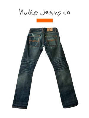 Nudie Jeans Selvage Grim Trim - Ett par Selvage Grim Trim Nudie Jeans i storlek 28/32. Måtten finns nedan. Bra skick, lite slitage/repa i grenen. Se bild 4!  Mått: Midja 39 cm - Grenhöjd 27,5 cm - Lårvidd 25 cm - Innerbenslängd 78 cm - Ytterbenslängd 102 cm - Benöppning 21 cm