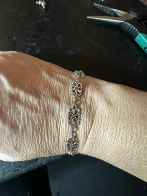 Silverfärgat armband med blommor - Snyggt armband i silverfärgad metall med flera länkar formade som blommor. Blommorna har små detaljerade pärlor i mitten och armbandet har en klassisk, bohemisk vibe. Perfekt accessoar för dig som gillar unika smycken med fina detaljer.