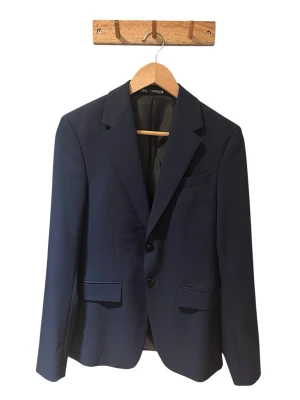 Mörkblå kavaj med byxor - Snygg mörkblå kavaj med byxor. Kavajen har två knappar framtill, klassisk krage och fickor med lock. Fodrad insida och stilren design som funkar till många olika looks. Perfekt för dig som gillar en tidlös och clean stil. Kostymen är från Zara. Skriv vid fler frågor