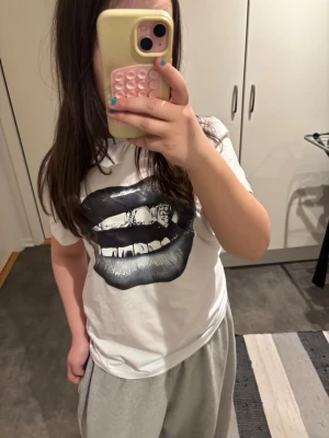 Vit t-shirt med svart läppar-tryck - Säljer en vit t-shirt med ett stort svart tryck av läppar och tänder på framsidan. T-shirten har korta ärmar och en klassisk passform. Perfekt för dig som vill sticka ut med en cool och edgy stil. Passar till hiphop stilar och hiphop- dansklasser❤️ 