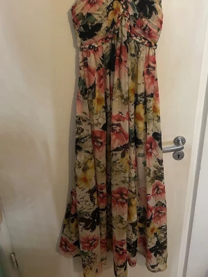 Blommig långklänning med flätade band - Långklänning med blommigt mönste. Klänningen har flätade axelband och detalj framtill, samt en luftig och flowy passform. Perfekt för varma dagar och sommarens alla tillfällen.