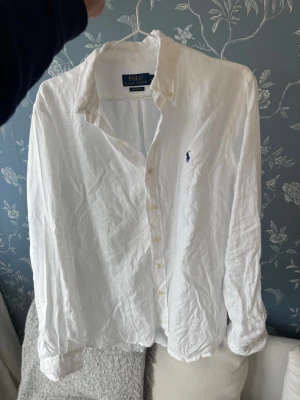 Vit linneskjorta från Polo Ralph Lauren - Klassisk vit skjorta i linne från Polo Ralph Lauren med blå broderad logga på bröstet. Skjortan har lång ärm, knappar framtill och en avslappnad passform. Perfekt för en stilren och fräsch look. Storlek M sitter som L. Inget syn på användning helt nyskick, endast testad. Ej lappar kvar.