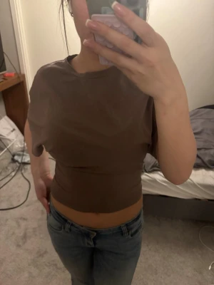 Brun croppad topp med kort ärm - Snygg brun croppad topp med korta ärmar och rund hals. T-shirten har en tight passform och är tillverkad i mjukt bomullsmaterial. Perfekt att matcha med jeans eller kjol för en trendig look.