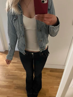 Ljusblå klassisk jeansjacka - Snygg ljusblå jeansjacka med klassisk passform och knäppning framtill. Jackan har två bröstfickor med lock och knappar samt sömdetaljer som ger en tidlös look. Perfekt att slänga över en t-shirt för en avslappnad stil eller att ha en finare topp under för en festligare look.