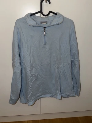 Ljusblå hoodie från Pure Wear - Ljusblå hoodie med halv dragkedja framtill och huva. Tillverkad i mjukt bomullsliknande material och har en avslappnad passform med långa ärmar. Perfekt för en chill och enkel stil.