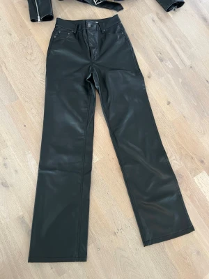 Svarta skinnbyxor från Zara, stl 34 - Snygga svarta skinnbyxor från Zara med raka ben och hög midja, stil 34. Byxorna har klassisk femficksdesign och stängs med knapp och dragkedja. Perfekta för en trendig och stilren look. Superfint skick, som nya! 