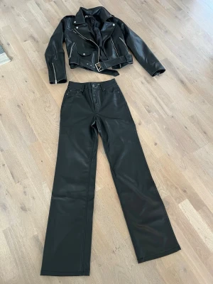 Svart skinnjacka (stl M) med bälte och skinnbyxor (stl 34)från Zara, stl S - Snygg svart skinnjacka (stl M) i klassisk bikerstil med silvriga dragkedjor och detaljer, samt matchande svarta skinnbyxor (stl 34), från Zara. Jackan har ett brett bälte i midjan och breda slag. Perfekt för dig som vill ha en edgy och trendig look. Säljer det dels som ett set för 800kr och dels var för sig för respektive 450kr/st. Är i superfint skick, använt endast ett fåtal gånger, som nytt! 