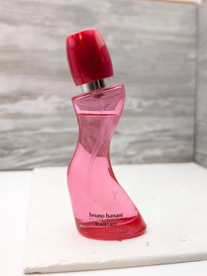 Bruno Banani Woman's Best parfym nästan full - En cool och unik parfymflaska från Bruno Banani, Woman's Best. Flaskan är i en snygg rosa färg med en vriden, feminin form och ett rött lock. Tillverkad i glas och plast, perfekt för dig som gillar trendiga och lekfulla dofter.
