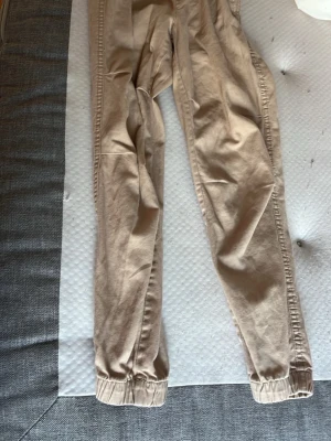 Beige joggers från H&M med resår - Beiga mjukisbyxor från H&M i joggermodell med elastisk midja och muddar vid bensluten. Byxorna har dragsko i midjan och är tillverkade i mjukt bomullsmaterial. Perfekta för en avslappnad och trendig stil.