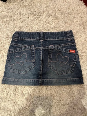 Jeanskjol med hjärtdetaljer - Superfin jeanskjol med dubbla knappar framtill och hjärtan på bakfickorna💕Kjolen är liten i storlek: 32 cm i midjemått rakt över & 29 cm lång