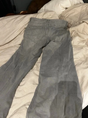 Gråa utsvängda jeans - Säljer ett par gråa jeans med utsvängda ben och hög midja. Jeansen har fram- och bakfickor samt synliga sömmar längs benen för en cool retrostil. Perfekta för dig som gillar en avslappnad men trendig look.