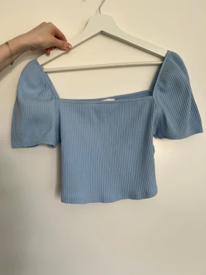 Ljusblå ribbad topp från H&M - Superfin ljusblå ribbad topp från H&M med puffiga korta ärmar och croppad passform. Toppen har en fyrkantig urringning och är perfekt för dig som gillar en trendig och söt stil. Tillverkad i mjukt material som känns skönt mot huden.