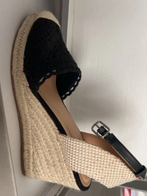 Svarta espadrille-wedges - Snygga espadrille-wedges med svart virkad ovandel, naturfärgad flätad platåsula och beige  runt hälen. Justerbart svart spänne i läderimitation. Köpt på din sko. Helt oanvända! Säljer för de aldrig kom till använding <3