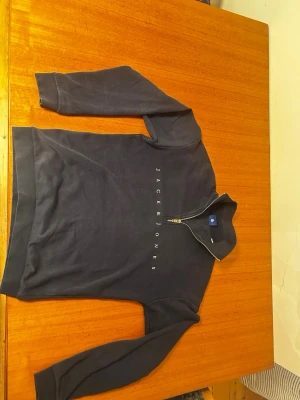 Mörkblå halfzip från Jack & Jones - Mörkblå sweatshirt med halv dragkedja från Jack & Jones. Tröjan har vit logotyptext över bröstet, ribbade muddar vid ärmslut och nederkant samt en avslappnad passform. Perfekt för en casual look och enkel att matcha med jeans. Priset kan diskuteras 