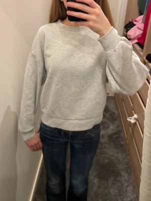 Ljusgrå basic sweatshirt - En enkel och stilren ljusgrå sweatshirt med rund hals och ribbade muddar vid ärmslut och nederkant. Tröjan har en avslappnad passform och är tillverkad i mjukt sweatshirtmaterial, perfekt för en casual look.