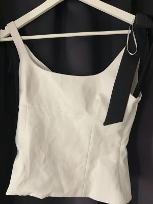 Vit axelbandslös topp med svart rosett - Säljer en festlig svart vit topp från Zara i storlek S med två Svarta Rosetter på Axelbanden 🤩 säljer då den aldrig riktigt kommit till användning därav Använd endast 1 gång🥰💐 skicka vid fler Frågor annars är det bara att köpa !❤️