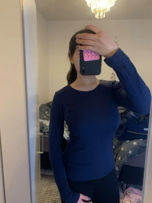 Mörkblå långärmad topp - En enkel och stilren mörkblå långärmad topp med rund halsringning. Passformen är slim och materialet är mjukt och stretchigt. Perfekt att matcha med jeans eller kjol för en clean look.