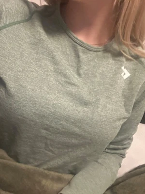 Grön långärmad träningströja - Snygg grönmelerad långärmad träningströja från lager 157. Tillverkad i ett mjukt och stretchigt funktionsmaterial som andas. Tröjan har rund halsringning och diskret logga på bröstet. Perfekt för träning eller aktiva dagar.