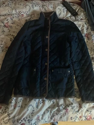 Svart quiltad jacka från CRW XS - Snygg svart quiltad jacka från CRW med tryckknappar framtill och två fickor med knappstängning. Jackan har hög krage och kontrastfärgade kanter. En ridjacka, kommer inte ihåg när den köptes. Pris går att diskutera.