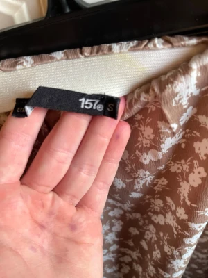 Beige blommig kjol från 157 - Söt beige kortkjol från 157 med vitt blommönster. Kjolen har en lätt utsvängd form och är gjord i ett mjukt, tunt material som känns skönt mot huden. Perfekt för dig som gillar en feminin och avslappnad stil.