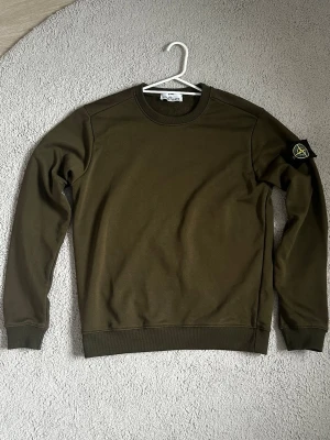 Olivgrön sweatshirt från Stone Island - Den olivgröna Stone Island tröjan i storlek M passar även storlek S. Tröjan är gjord i mjukt och skönt material med en enkel design och Stone Islands märke på ärmen. Jag är aktiv hela tiden ✅och fraktar tröjan samma dag eller nästa🚚📦 Den är i bra skick och perfekt för både vardag och finare tillfällen. Tveka inte o fråga 🙋‍♂️ Ett utmärkt tillskott till din garderob!👌🤩