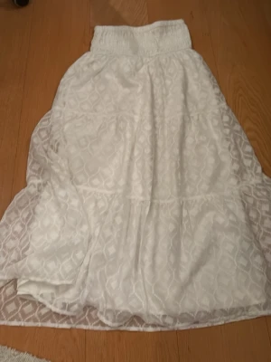 Vit långkjol från Gina Tricot - Säljer en vit långkjol från Gina Tricot med elastisk midja och diskret mönster i tyget. Kjolen har ett tunt, luftigt material och faller snyggt. Perfekt för dig som gillar en enkel men ändå stilren look. Väldigt stor i storleken och passar mig som har xs! Jättegullig till på sommaren! Nästan helt oanvänd 