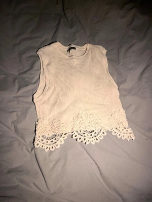 Beige ribbad linnetopp från Zara - Säljer en beige ribbad linnetopp från Zara med snygga spetsdetaljer längst ner. Toppen är ärmlös och har en croppad passform som ger en trendig look. Perfekt att matcha med höga jeans eller kjol för en cool outfit🫰🏽