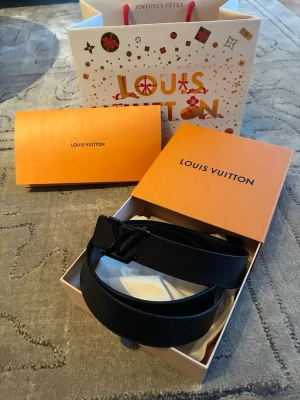 Svart Louis Vuitton skärp i skinn - Snyggt svart skärp från Louis Vuitton i äkta skinn med klassiskt LV-spänne i svart. Kommer i originalförpackning med dustbag och box. Perfekt accessoar för att lyfta vilken outfit som helst.