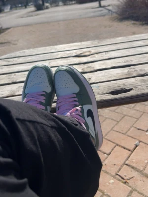 Nike Air Jordan 1 Mid gröna sneakers - Snygga Nike Air Jordan 1 Mid sneakers i grönt och vitt med svarta swoosh-detaljer och rosa skosnören. Klassisk siluett med perforerad tåbox och ikonisk Air Jordan-logga på sidan. Skorna har en vit mellansula och grön yttersula. Perfekta för dig som vill sticka ut. Orginal pris 3000kr, 1200 vid snabb affär 