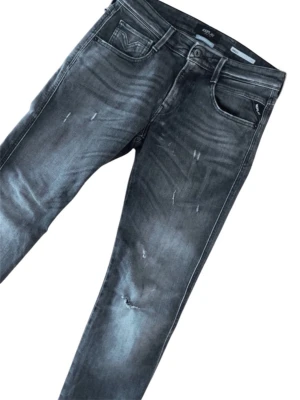 Grå slitna jeans från Replay - Säljer ett par grå jeans från Replay med slitna detaljer och tvättad look. Jeansen har fem fickor, raka ben och coola slitningar både fram och bak. Materialet är klassisk denim med stretch för extra komfort. Perfekta för en avslappnad streetstyle.