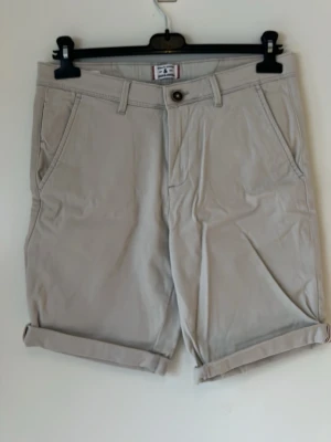 Beige shorts med uppvikta ben - Snygga beige shorts med uppvikta ben och klassisk passform från Jack&Jones. Shortsen har sidofickor fram, två bakfickor och bälteshällor. Perfekta för varma dagar och enkla att matcha med olika stilar.