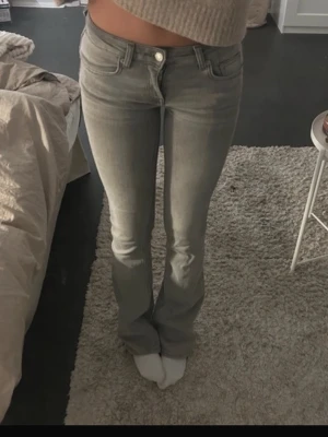 Grå bootcut jeans med låg midja - Säljer ett par gråa bootcut jeans med låg midja och klassisk femficksmodell. Jeansen har en snygg tvättad look och är tillverkade i stretchigt denimtyg för skön passform. Perfekta för dig som gillar en avslappnad men trendig stil.