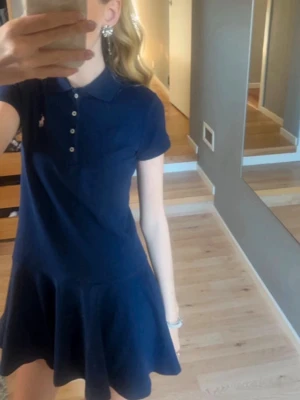 Polo Ralph Lauren klänning  - OBS! Storlek M-L i Barnstorlek (10-11 år), men passar XXS, kanske XS och har burits av mig när jag var 15. Modellen är stretch mesh polo dress nypris 1295kr på Zalando. Säljer en marinblå kort pikéklänning från Ralph Lauren med klassisk krage, knappar framtill och korta ärmar. Klänningen har en lätt utställd kjol och den ikoniska loggan broderad på bröstet. Perfekt för en sportig och stilren look. 